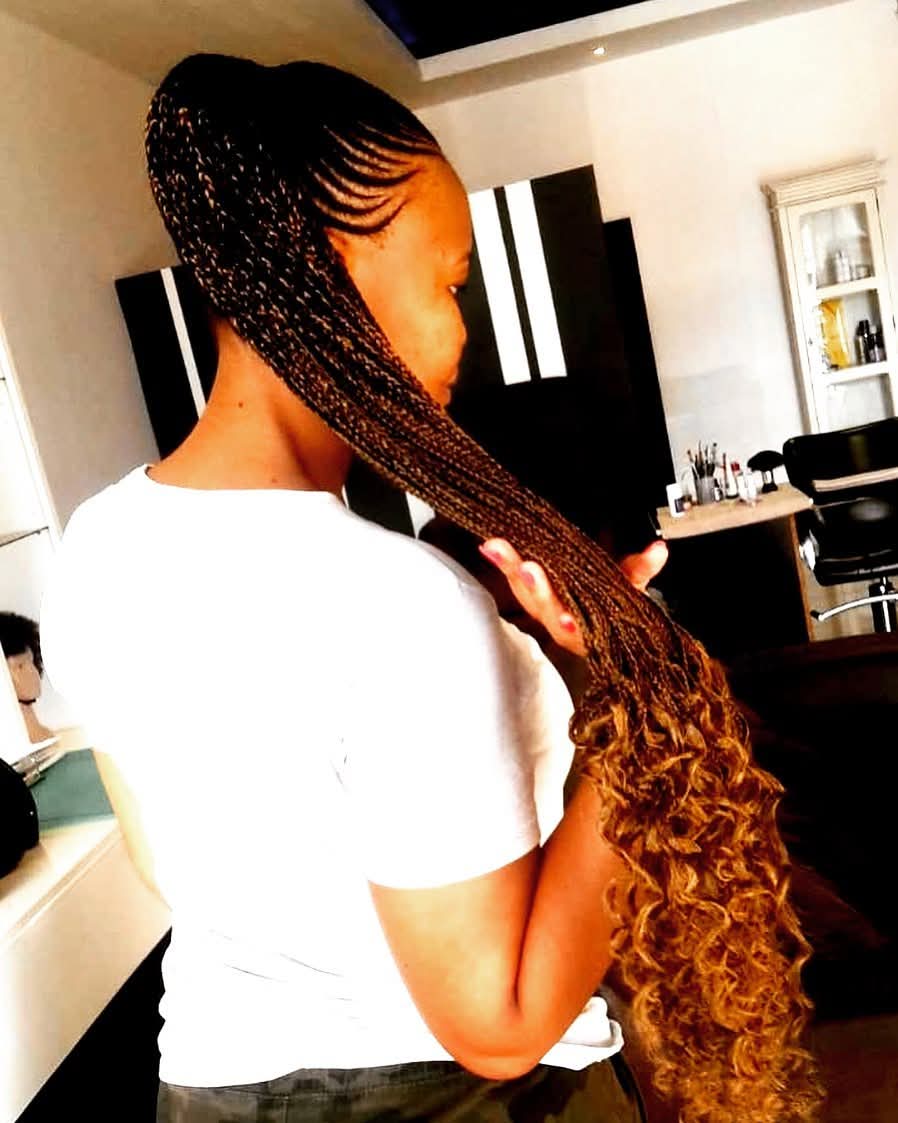 Sleek feed-in cornrows with caramel highlights flowing into curly ends